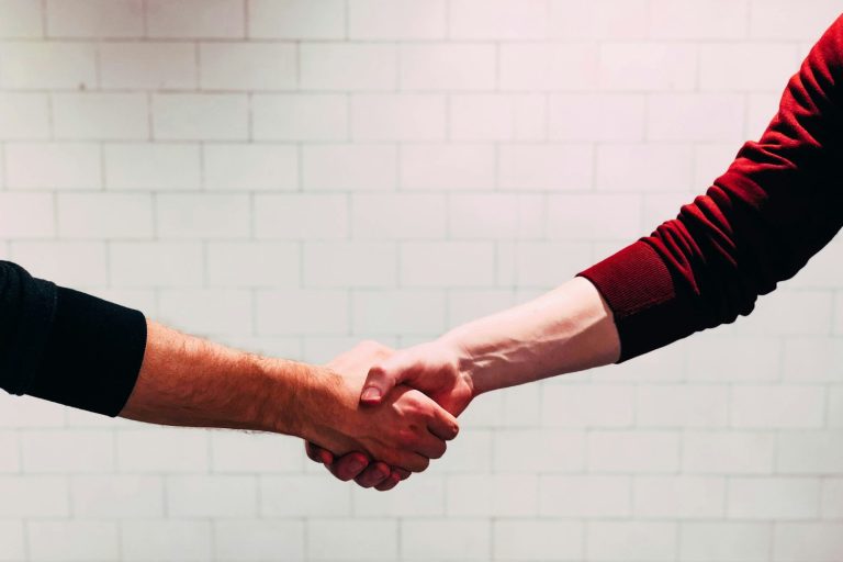 Two person shaking hands near white painted wall