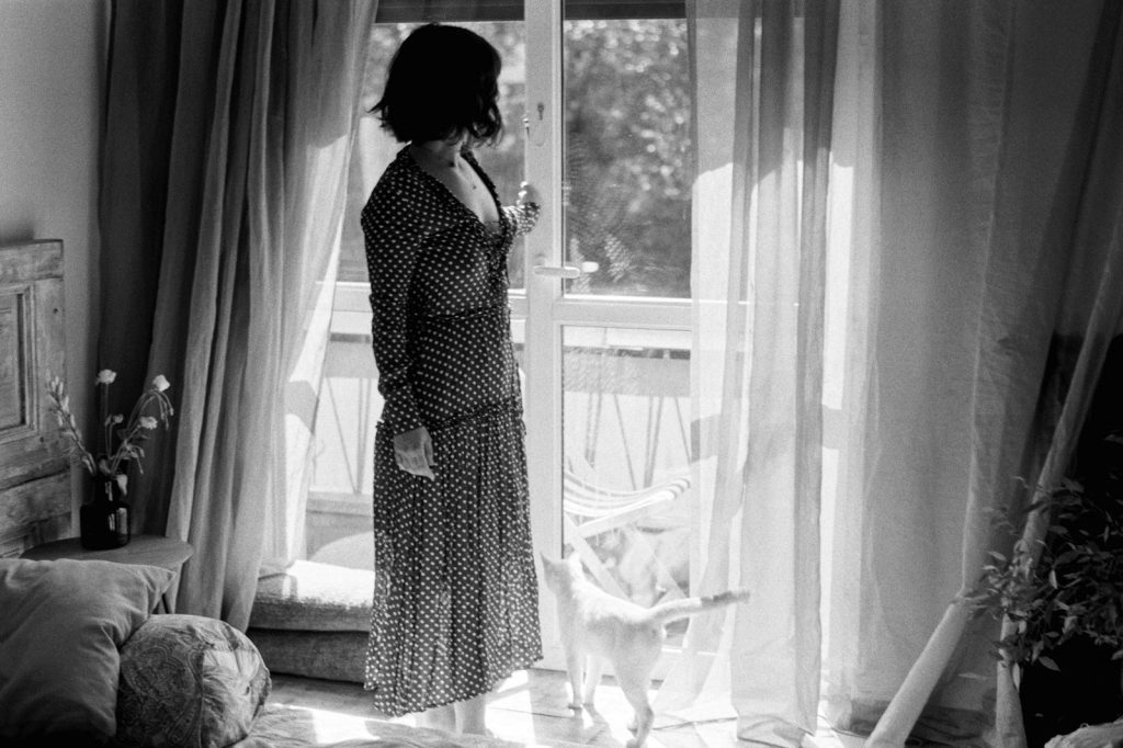 A woman standing in front of a window next to a cat