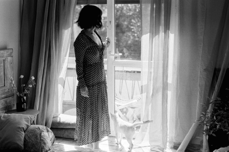 A woman standing in front of a window next to a cat