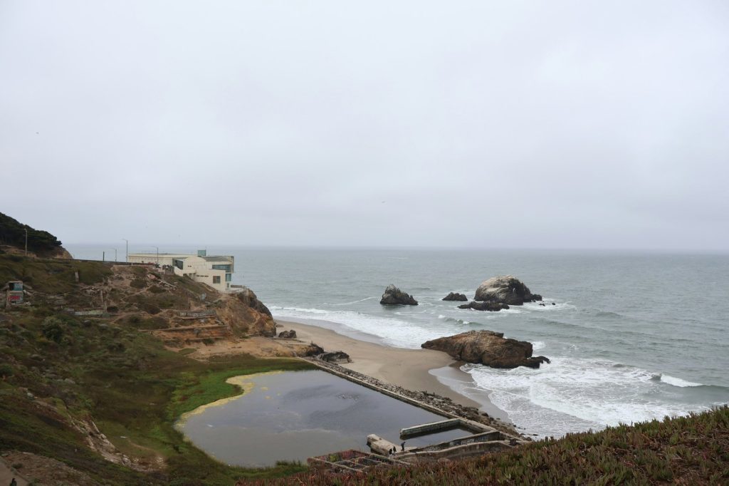 Ocean waves crash on a rocky beach with a building.
