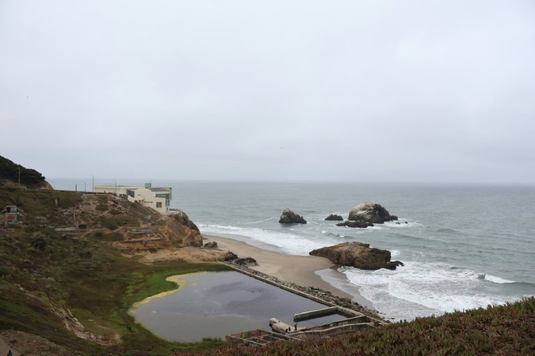 Ocean waves crash on a rocky beach with a building.
