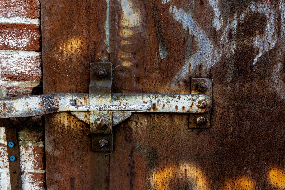 A heavily corroded metal door with a rusted latch, showing what happens when corrosion is allowed to propagate
